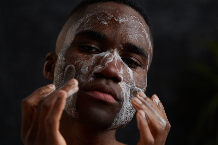 photo of a man washing his face with a facial cleanser and looking straight at the camera with a black background